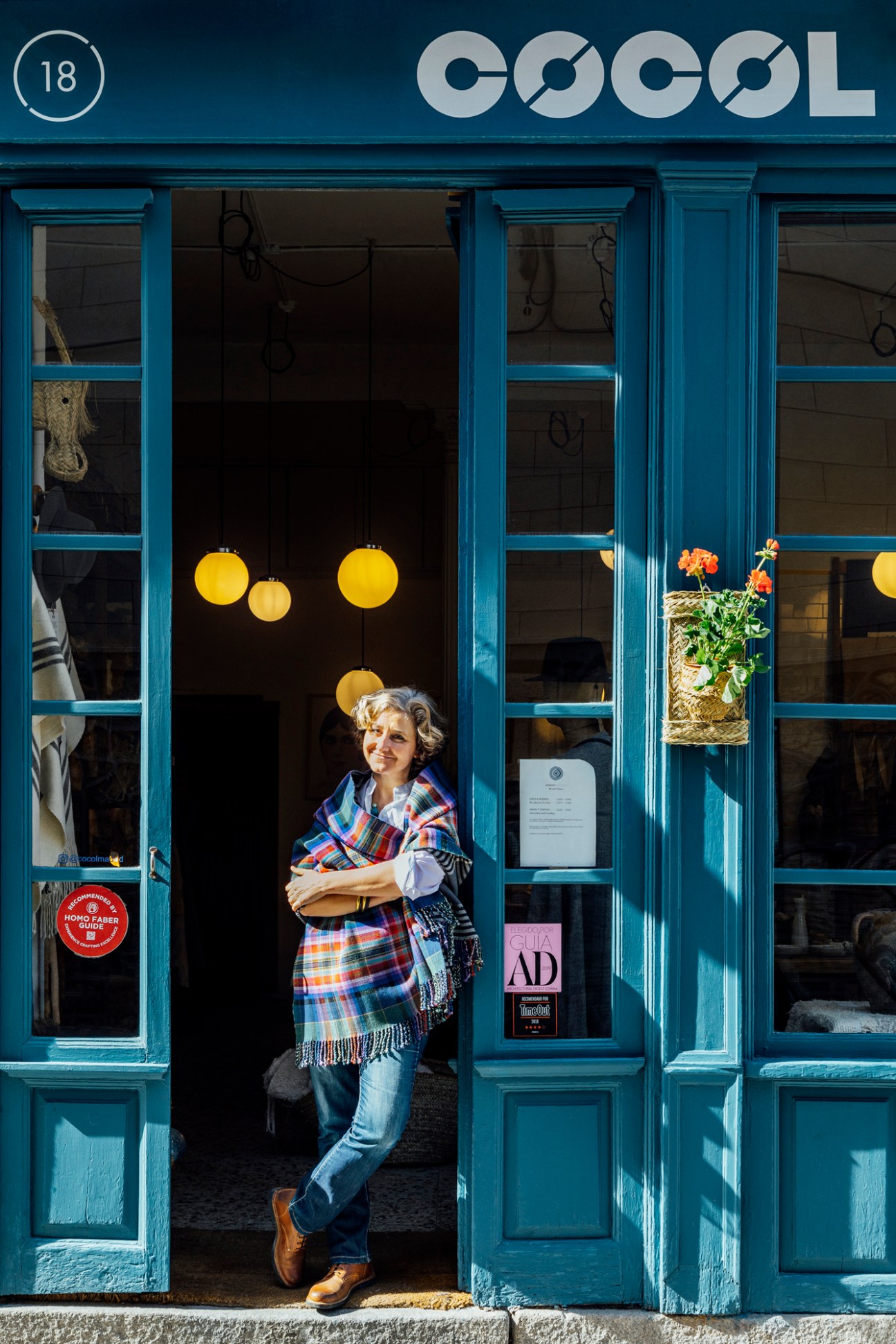 Woman in plaid shawl standing in blue-painted storefront doorway with COCOL signage