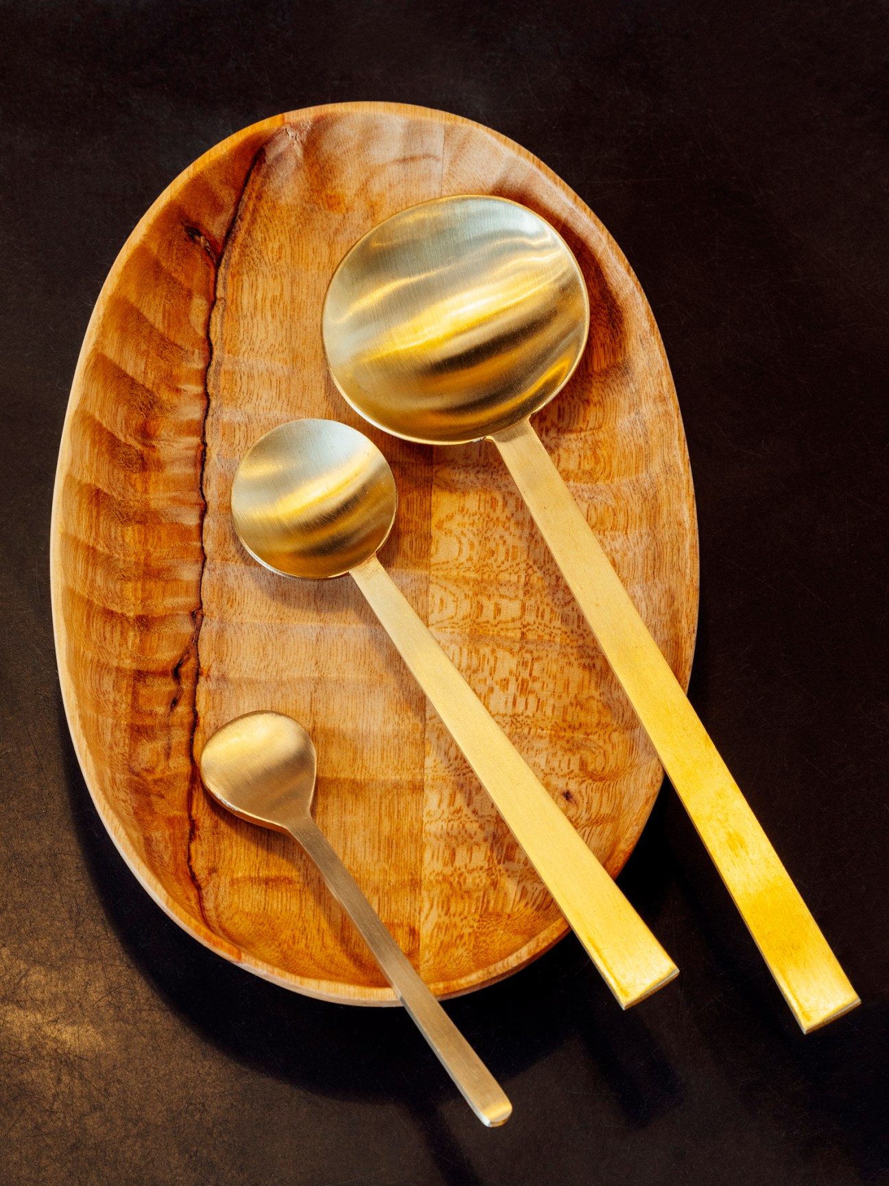 Brass serving spoons with long handles arranged on wooden cutting board