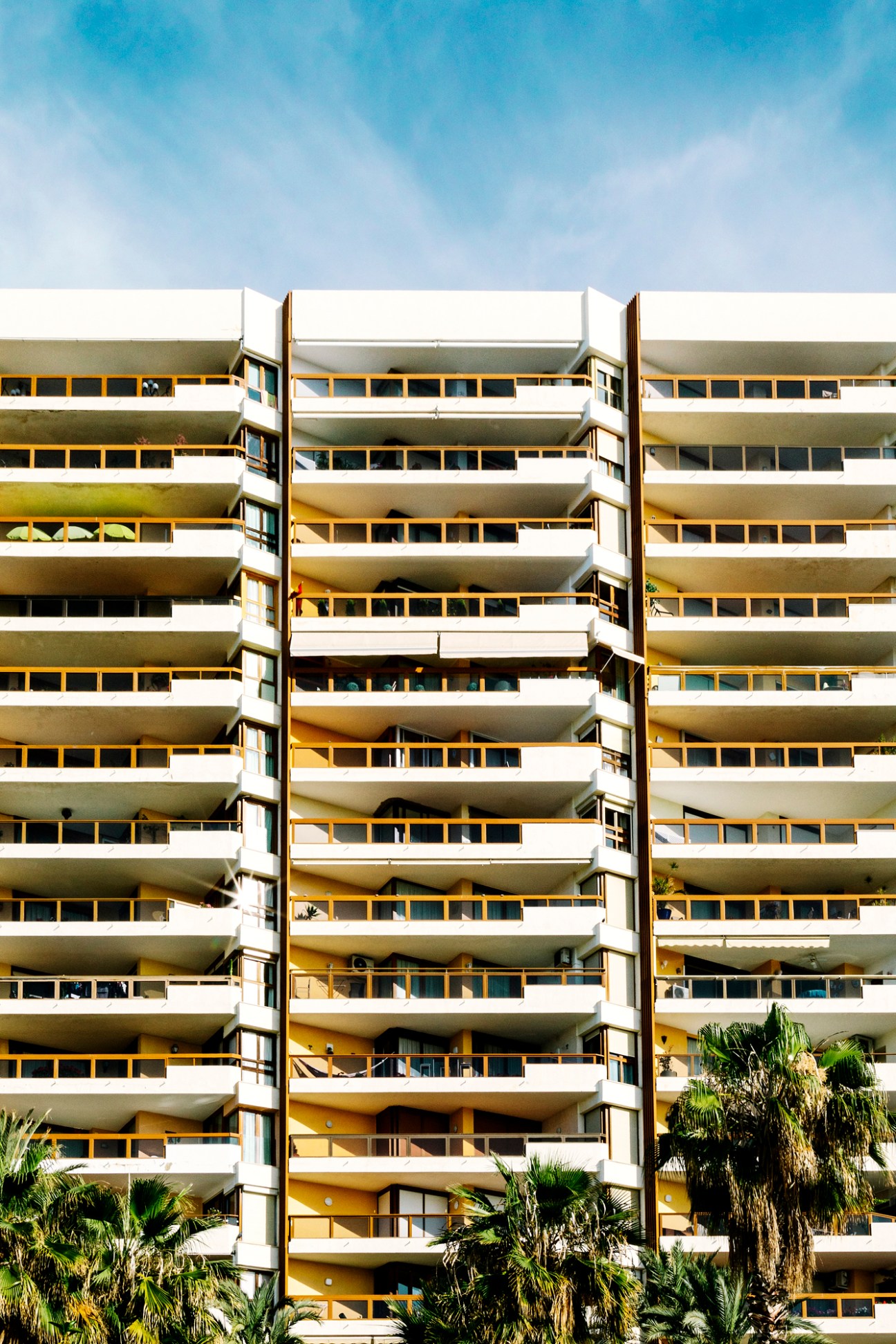 Modern residential apartment building with yellow-framed windows and white balconies against a blue sky.