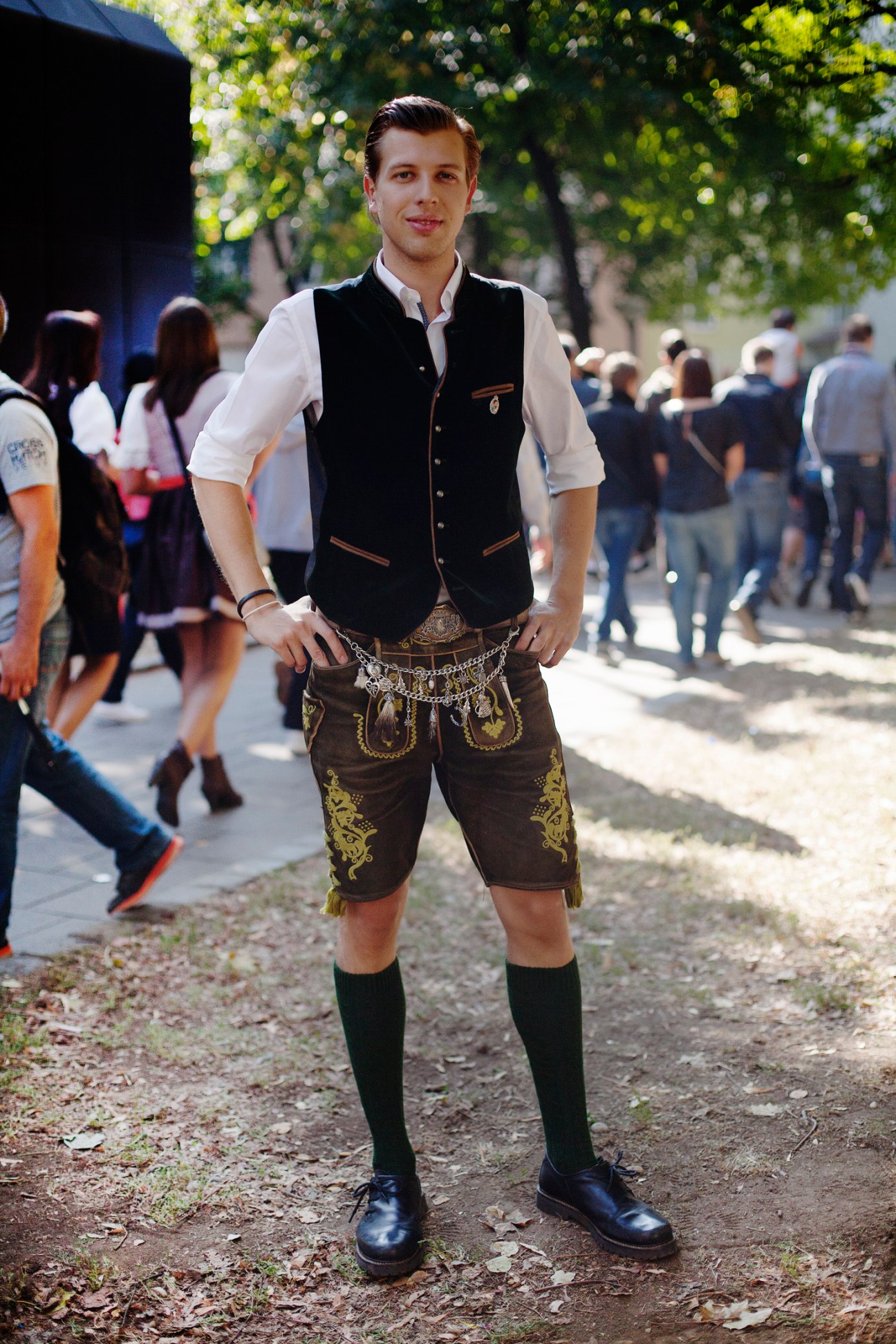 Young man in traditional Bavarian lederhosen outfit with embroidered brown shorts, black vest, white shirt and black socks.