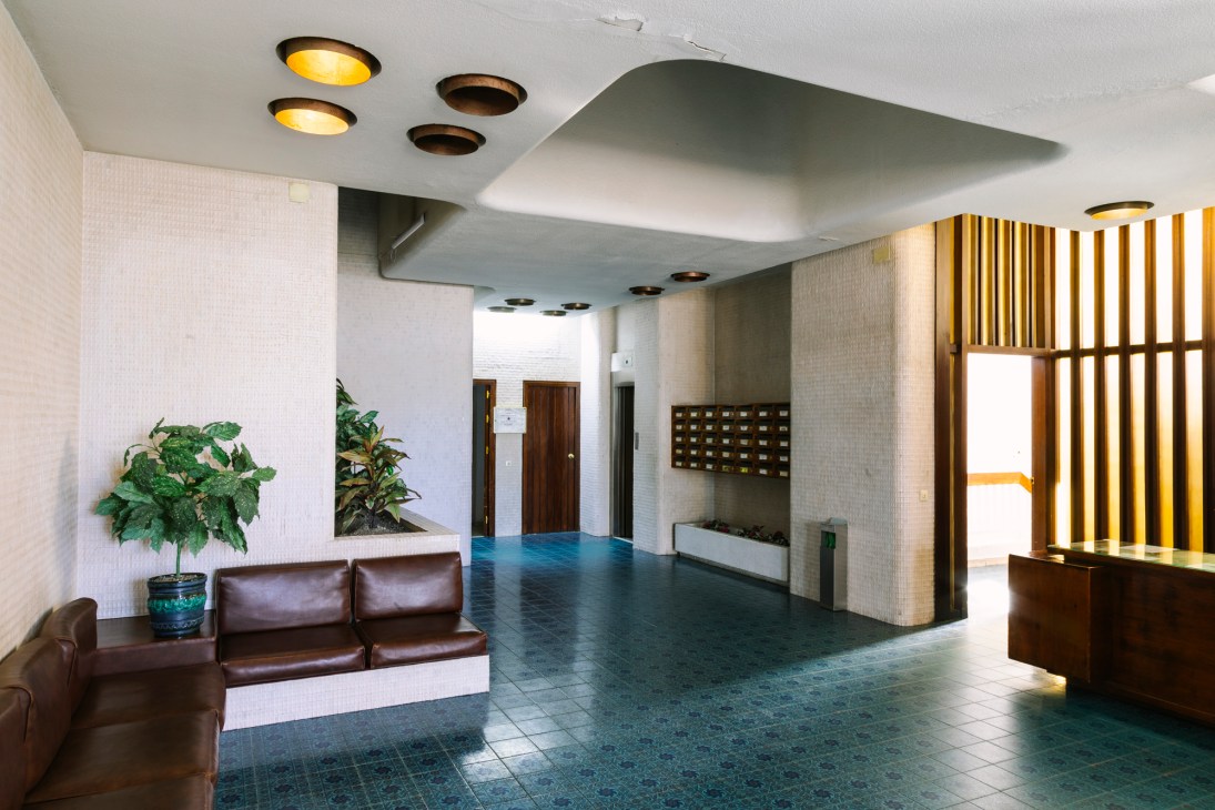 Modernist foyer with turquoise tiles, dark leather sofas, wooden mailboxes and recessed ceiling lights