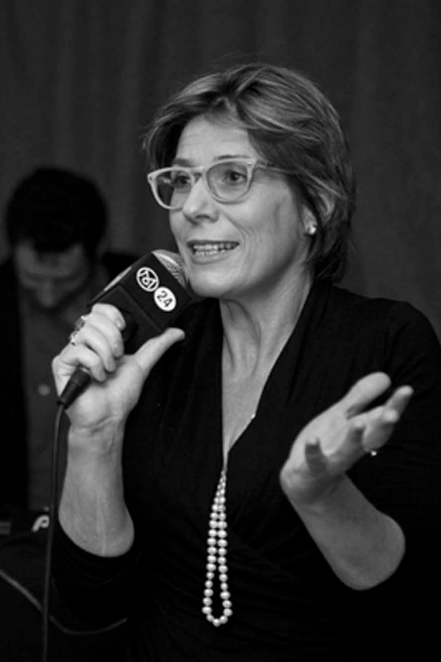 Presenter Georgina Godwin speaking into a microphone while wearing glasses and a pearl necklace