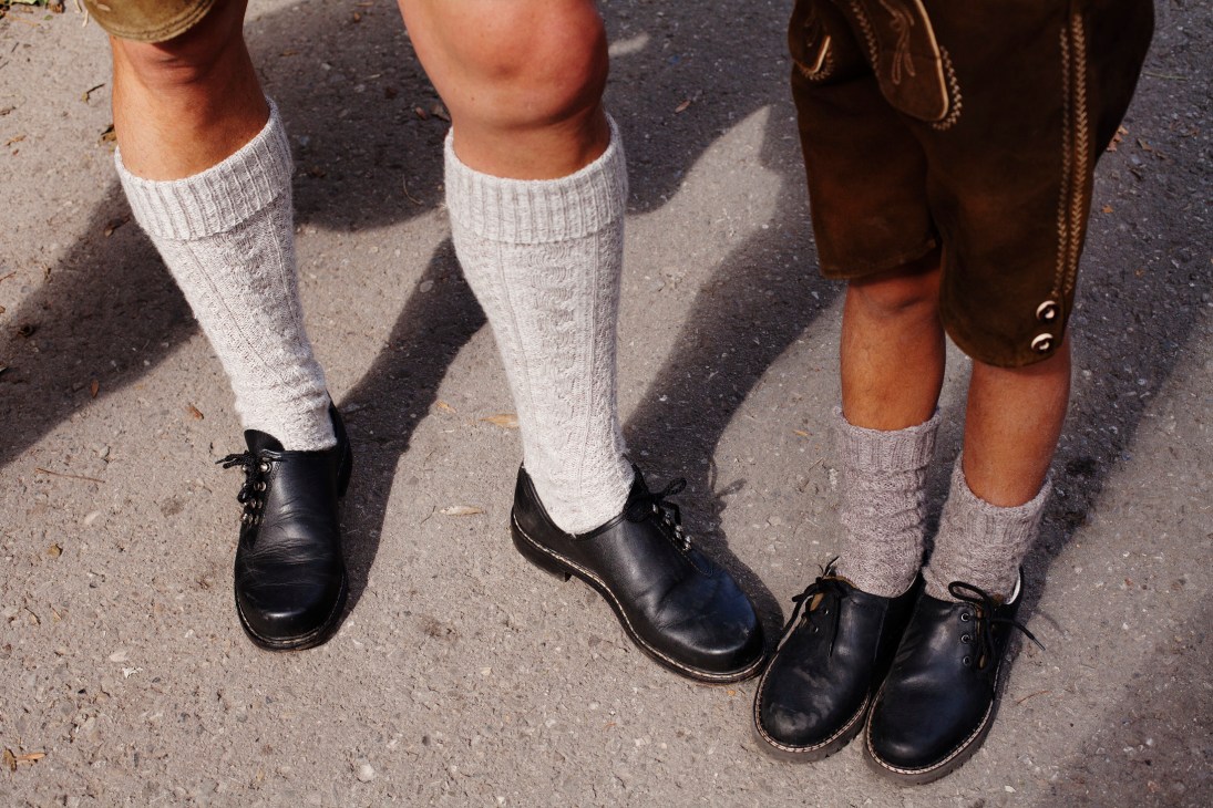 Three people wearing white cable-knit socks and black shoes stand on pavement.