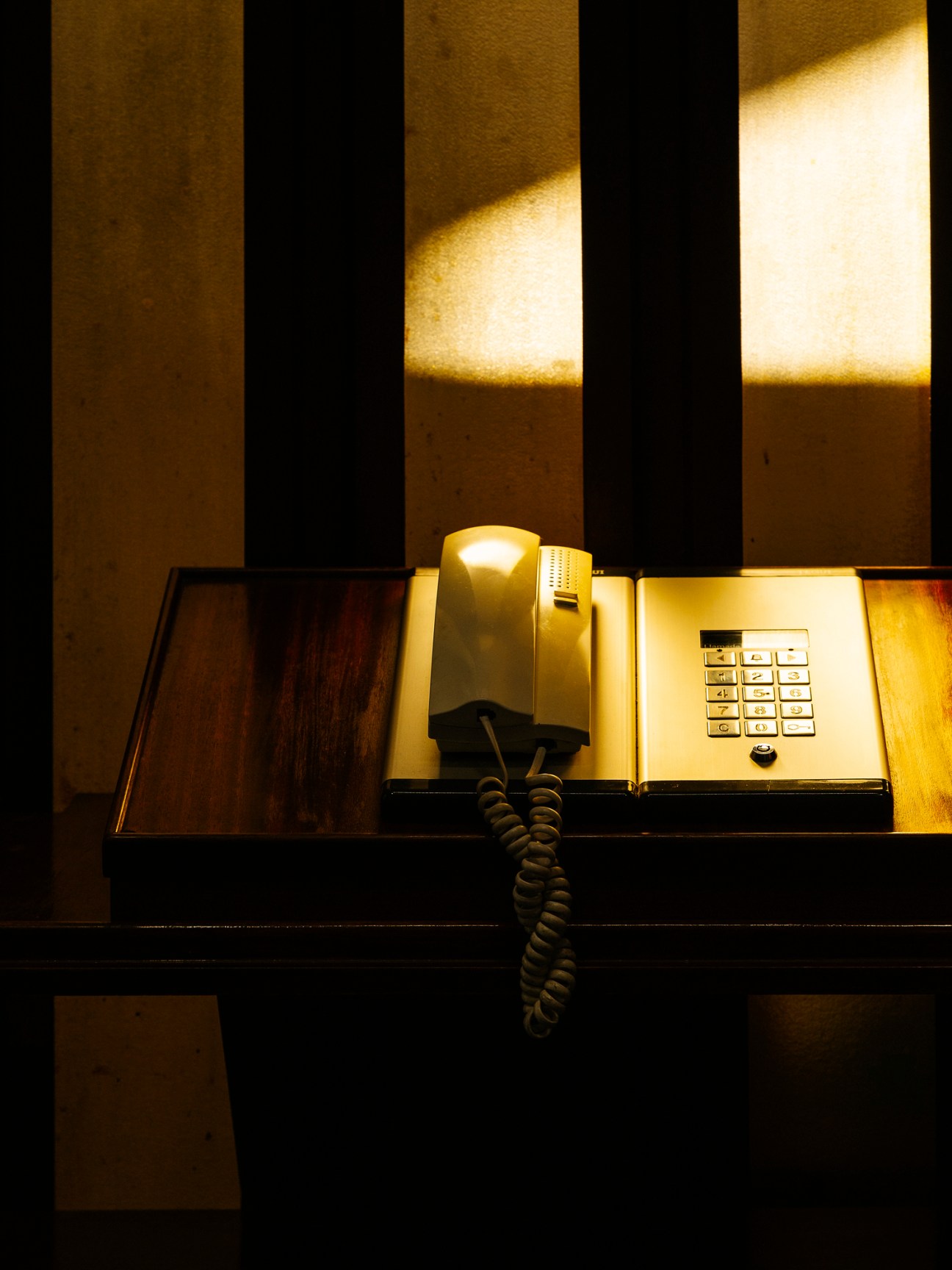 Vintage brass intercom and telephone mounted on a wooden panel with striped wall backdrop