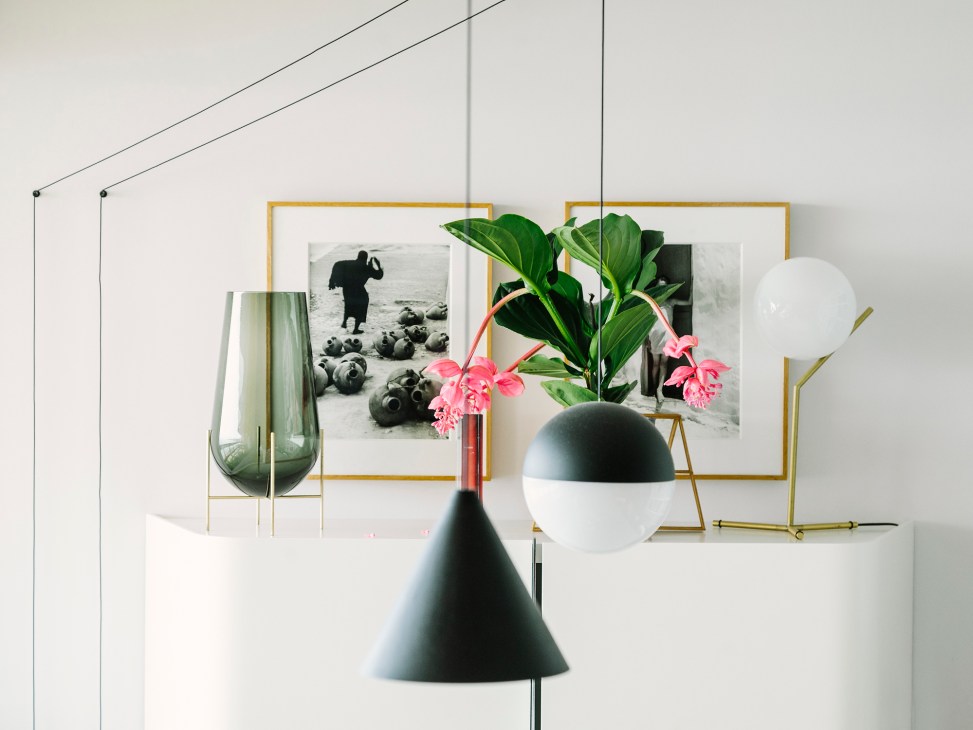 Modern interior with pendant lamps, potted plant with pink flowers, framed photographs, and green vase against white wall.