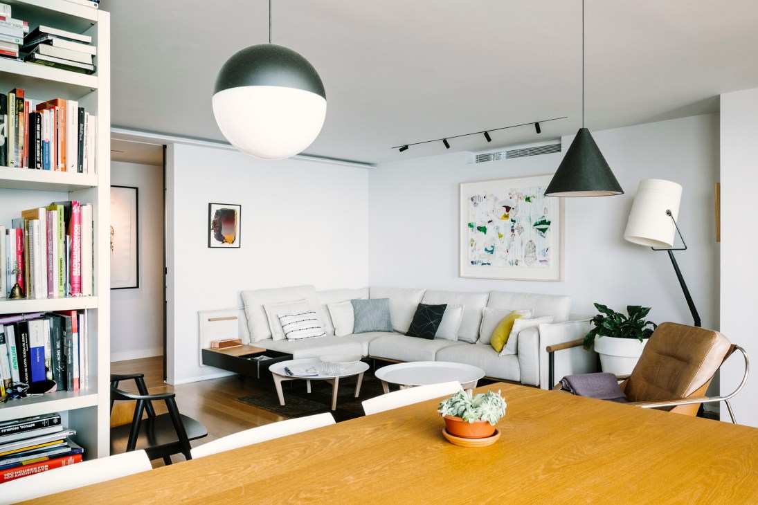 Modern living room with white sectional sofa, wooden dining table, pendant lights, and built-in shelving.