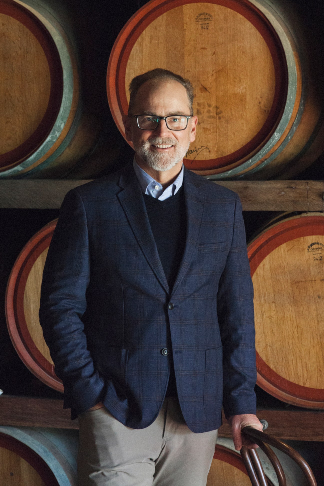 Sandalford CEO Grant Brinklow smiling in navy blazer standing in front of wine barrels
