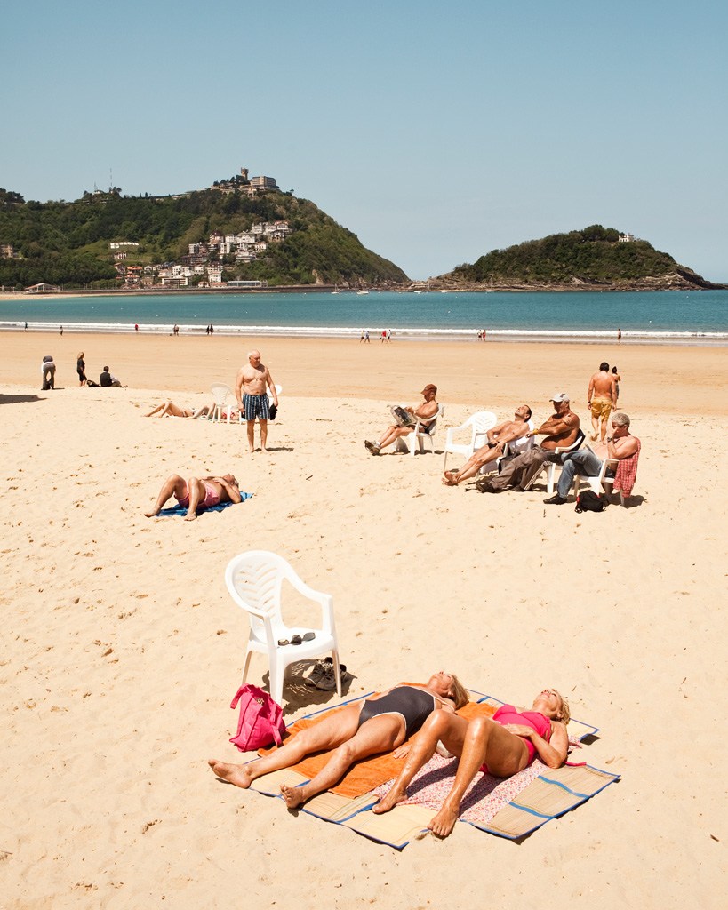 Beachgoers sunbathing and relaxing on golden sand at Playa de la Concha in San Sebastián.
