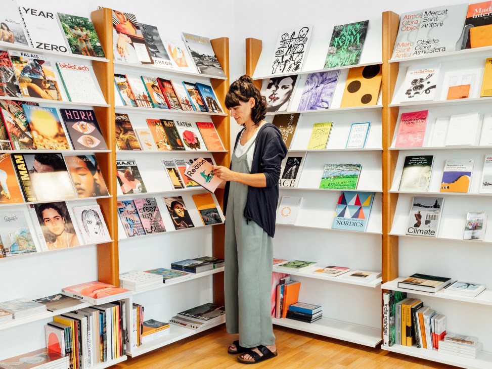Woman browsing magazines in Paperground bookstore with wooden shelving displaying colorful publications
