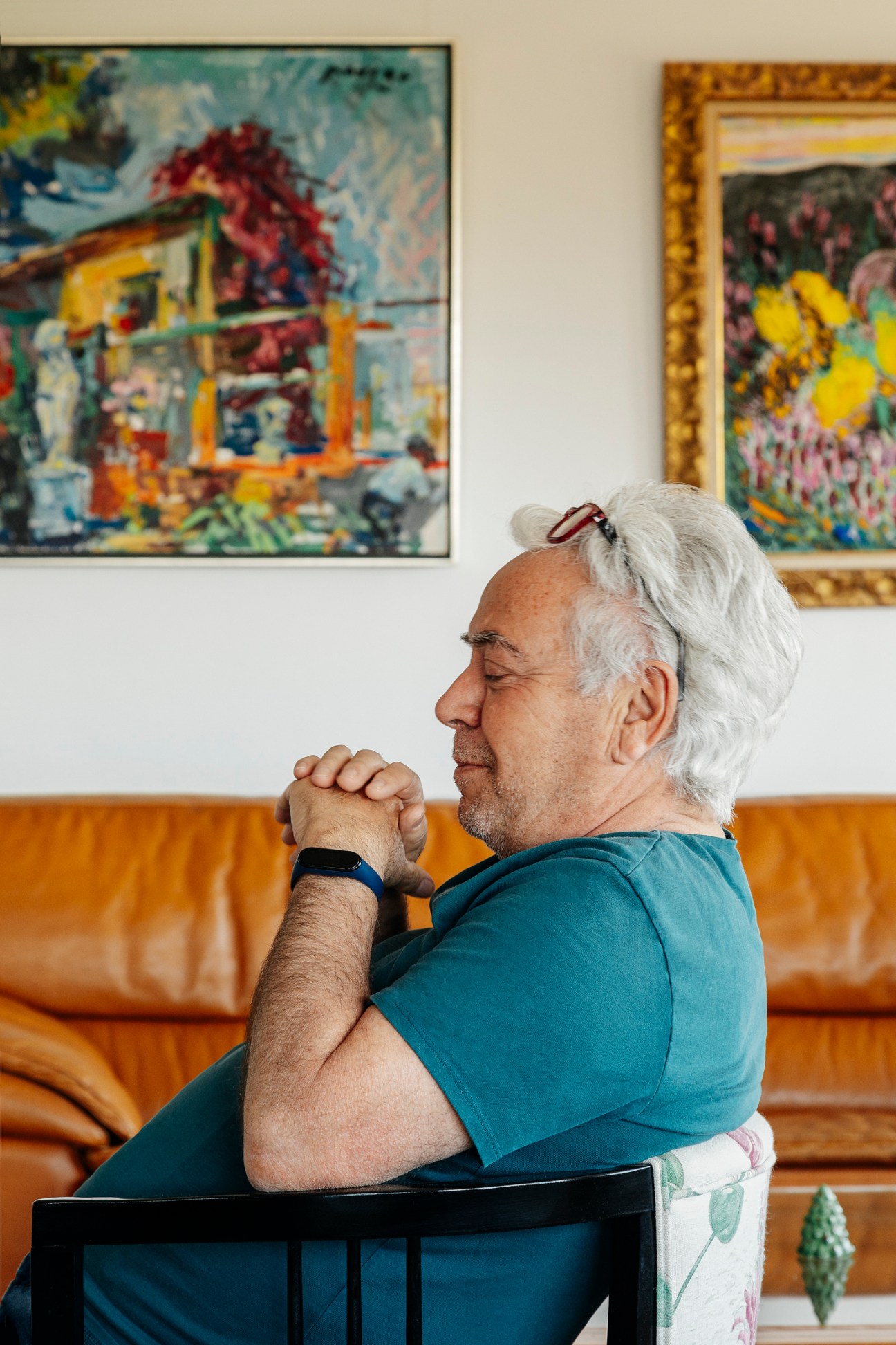 Pepe Cano sitting in profile in his apartment with hands clasped, colorful artwork visible on walls behind him