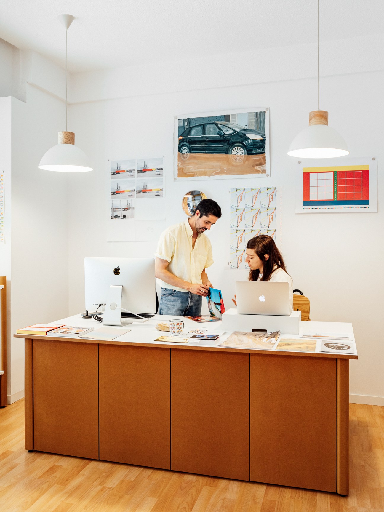 Woman with long dark hair working on laptop at wooden desk in bright modern studio space