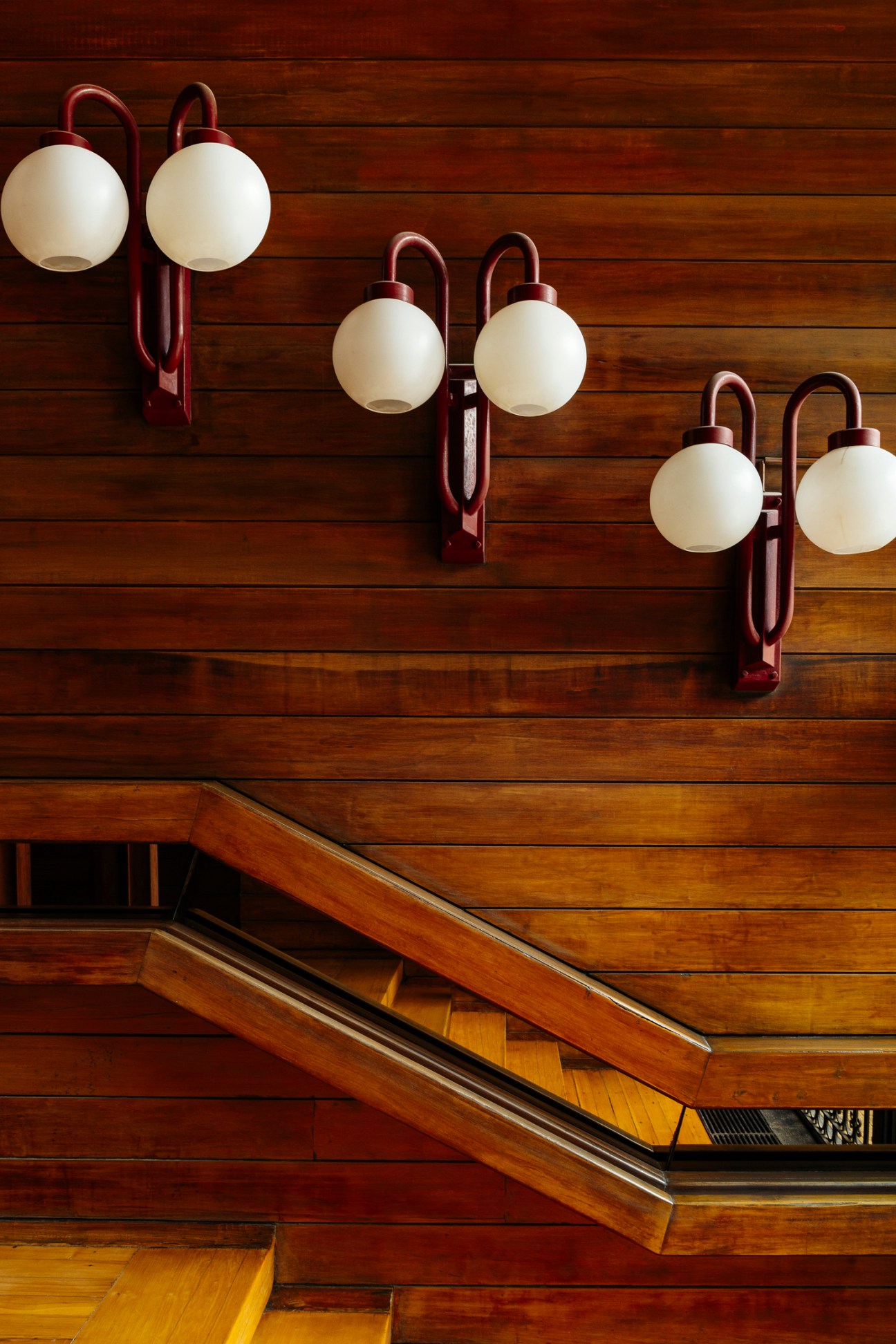 Modernist wall sconces with red metal frames and white spherical globes mounted on wood-paneled wall above staircase