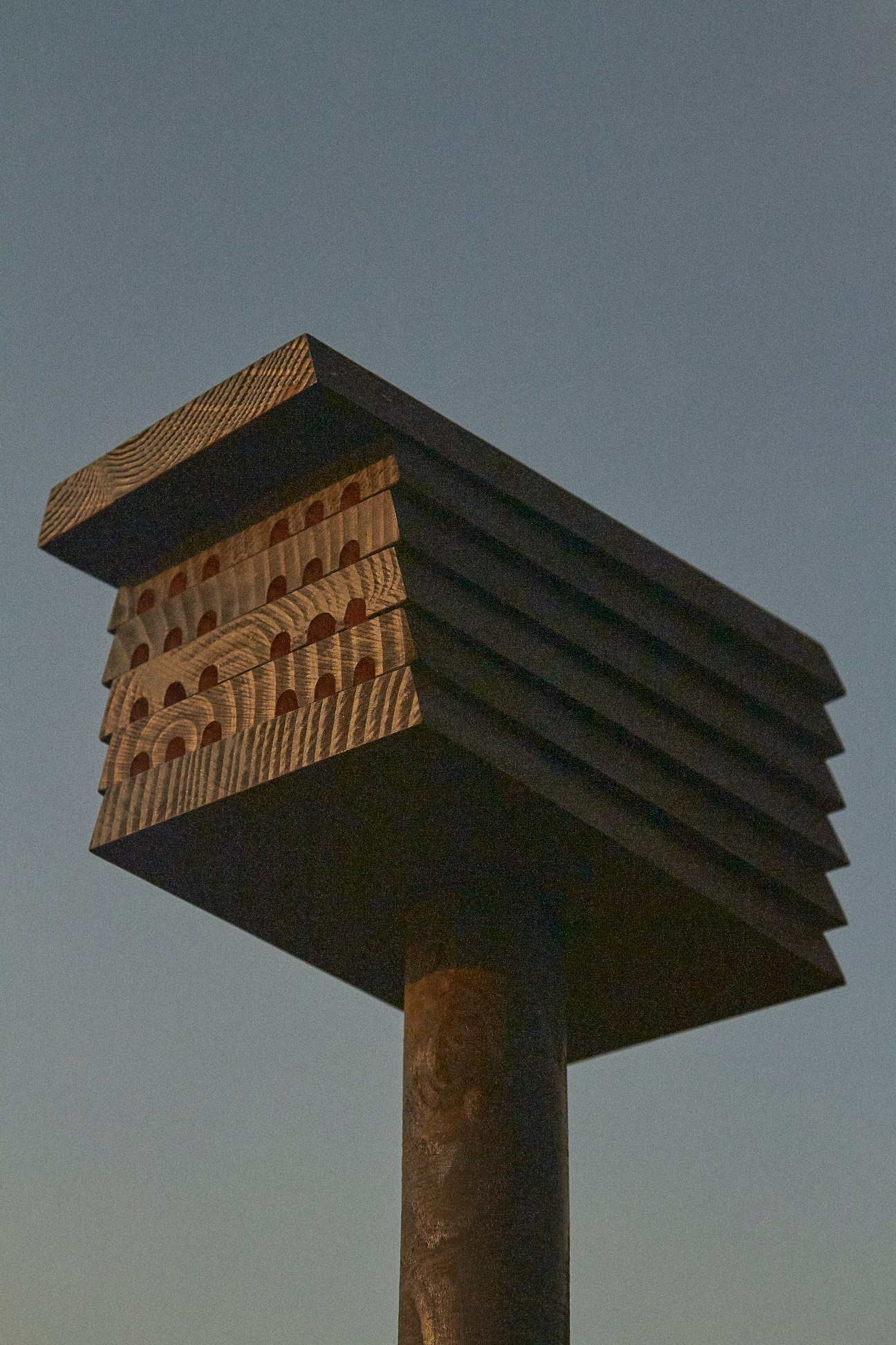 Minimalist wooden beehive shelter mounted on post against gray sky