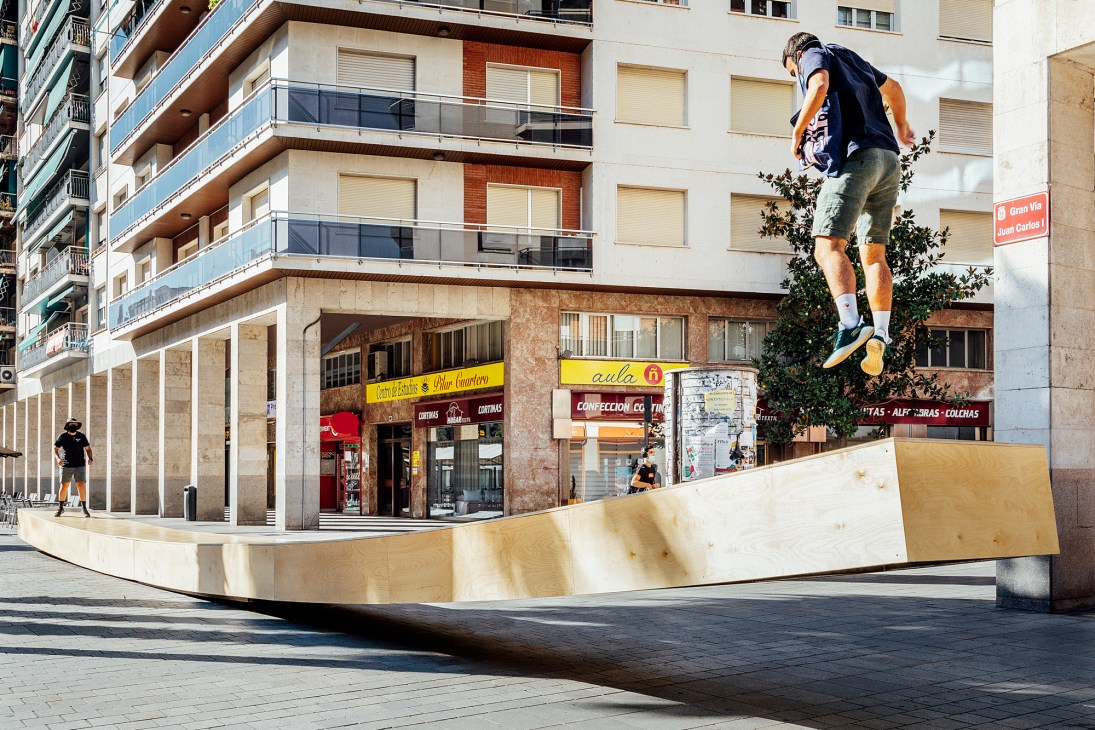 Person jumping on wooden bench installation 'Banquín' by Madrid-based architects Mecanismo in urban plaza