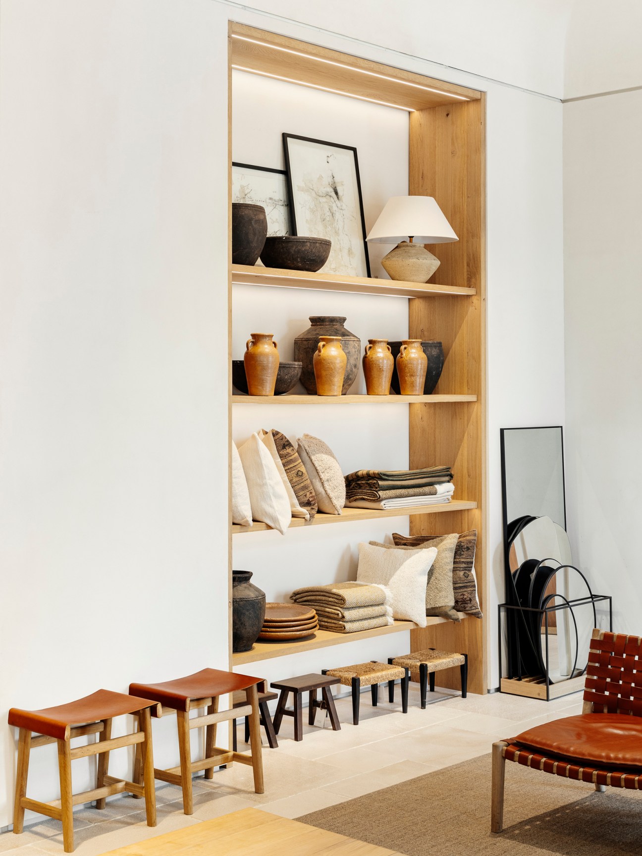 Built-in wooden shelving unit displaying pottery, books, textiles and decorative objects in apartment-style retail setting