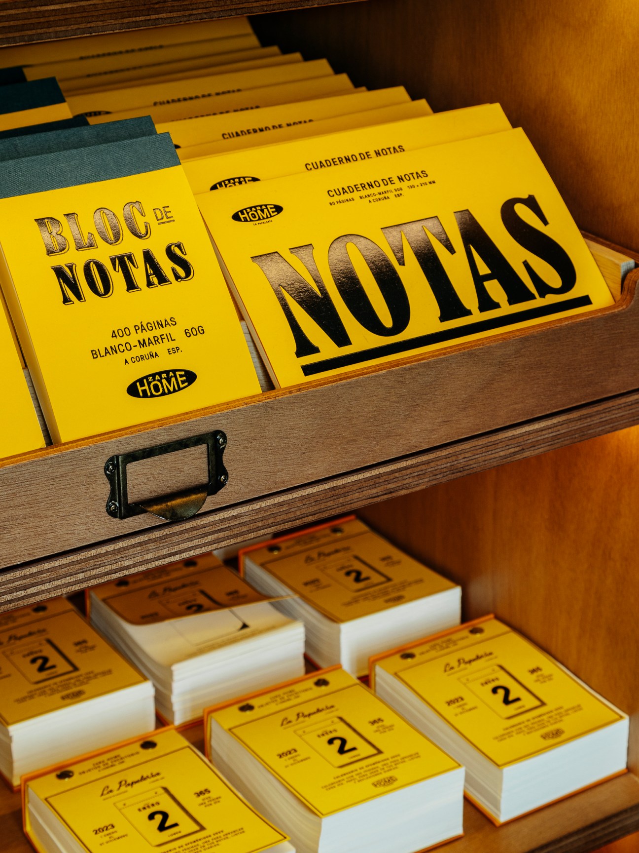 Yellow notebooks and calendars with Spanish text displayed in wooden drawer compartments