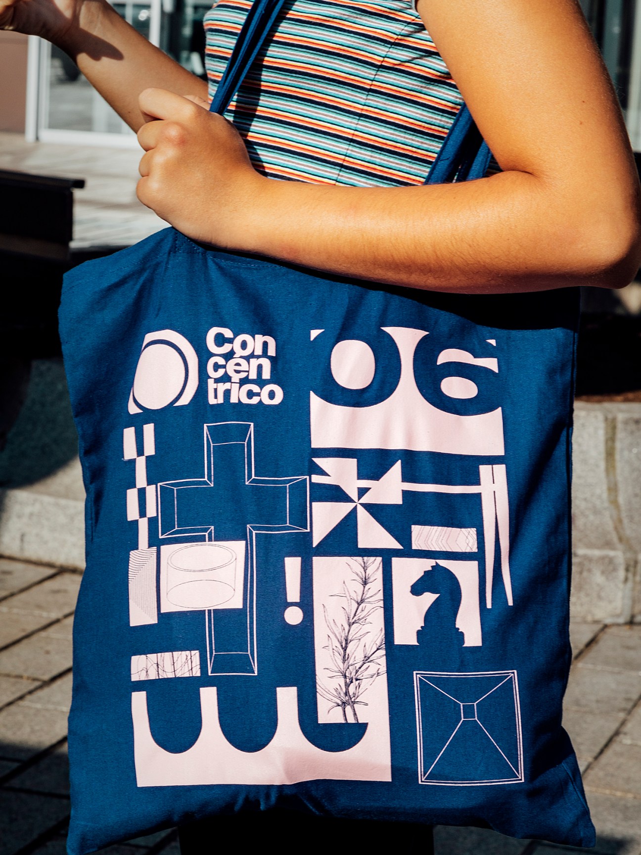 Person holding blue Concéntrico festival tote bag with white geometric design and text