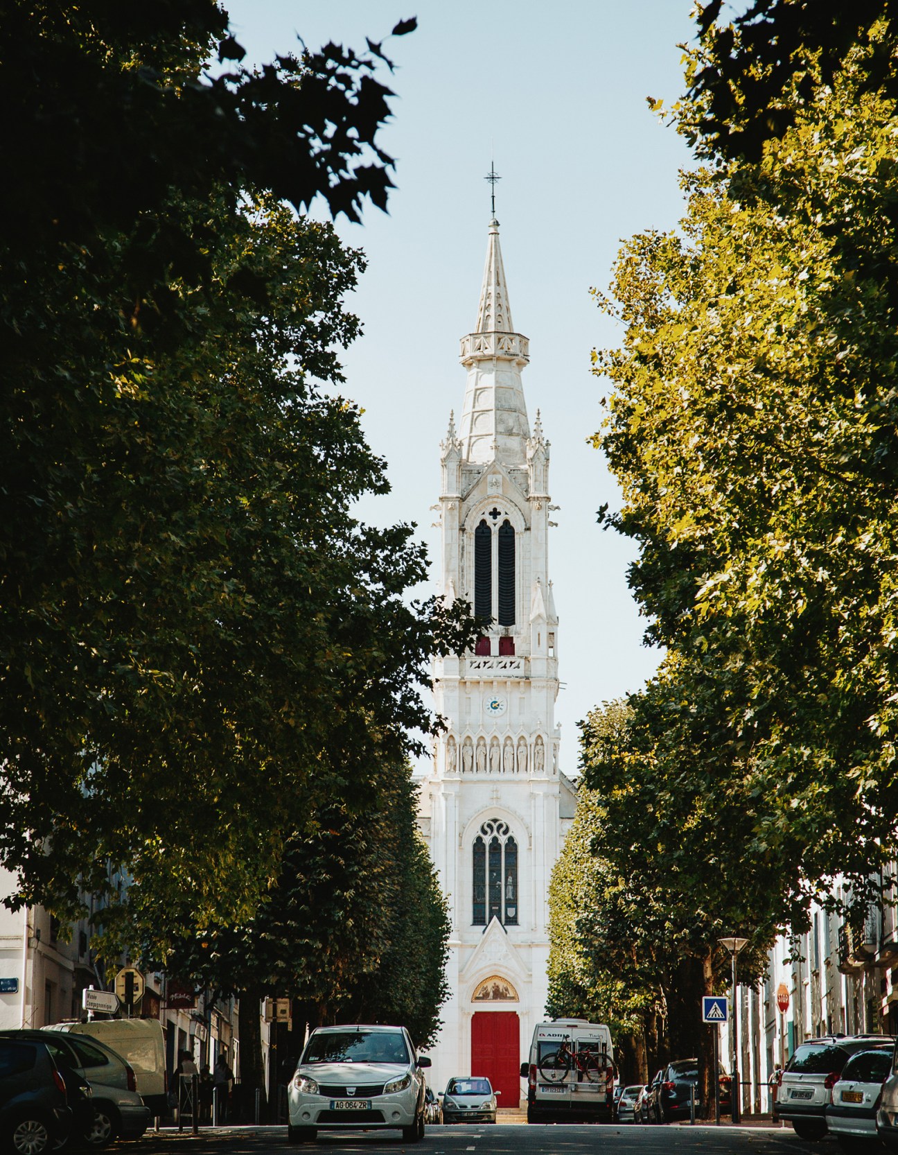 White neoclassical church tower with spire framed by tree-lined street in Nantes.