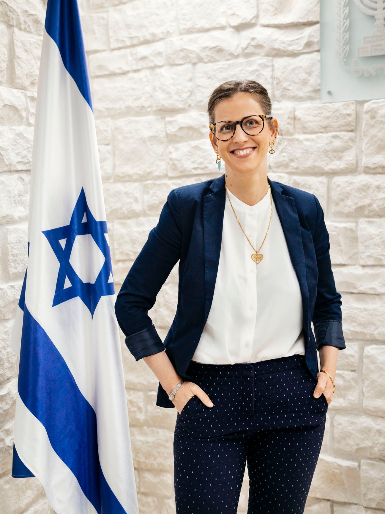 Shelly Hugler Livne, Israeli culture attaché in Spain, standing in business attire next to Israeli flag