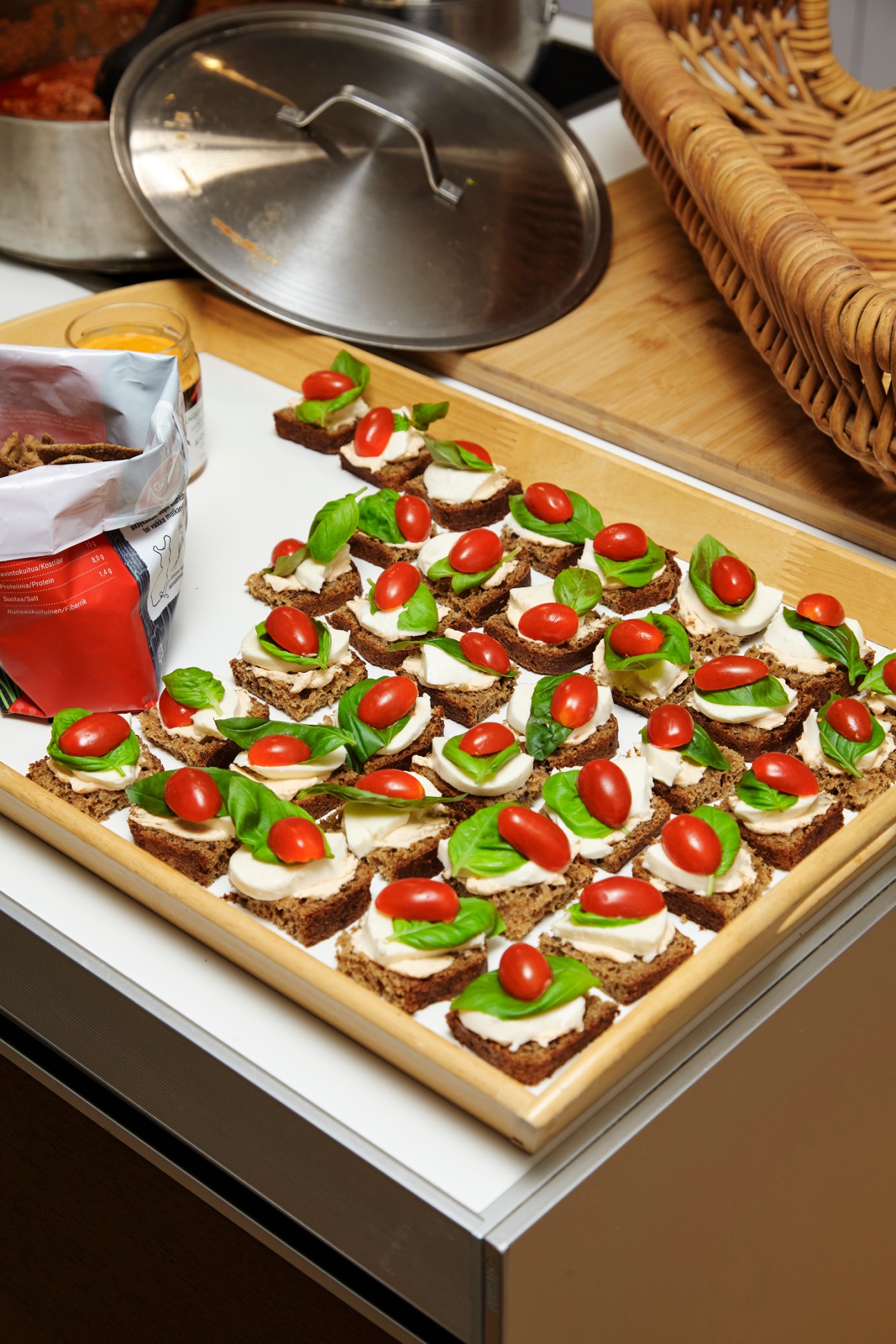 Small appetizers with white cream, cherry tomatoes and green herbs arranged on dark bread squares on a wooden tray