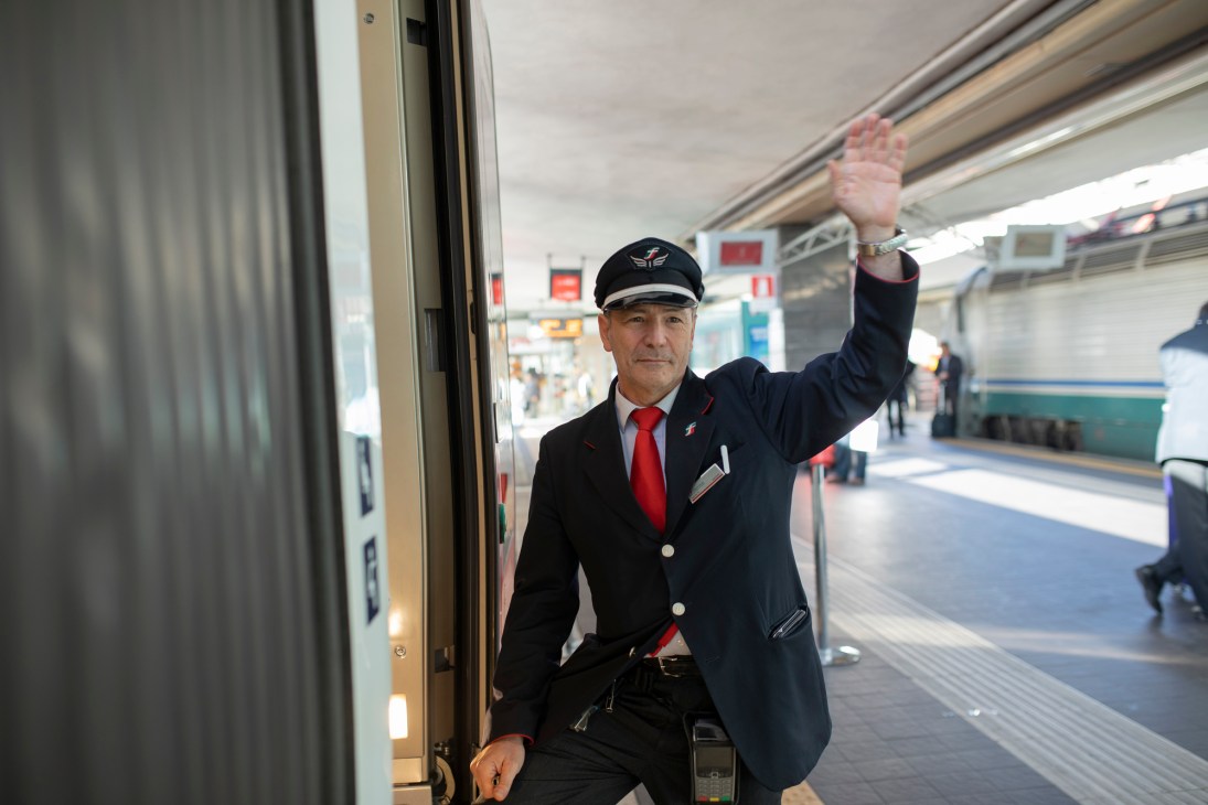 Train conductor in dark uniform and cap standing beside train door at platform station