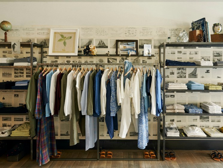 Open wardrobe system with hanging clothes and folded items on shelves against wallpapered walls