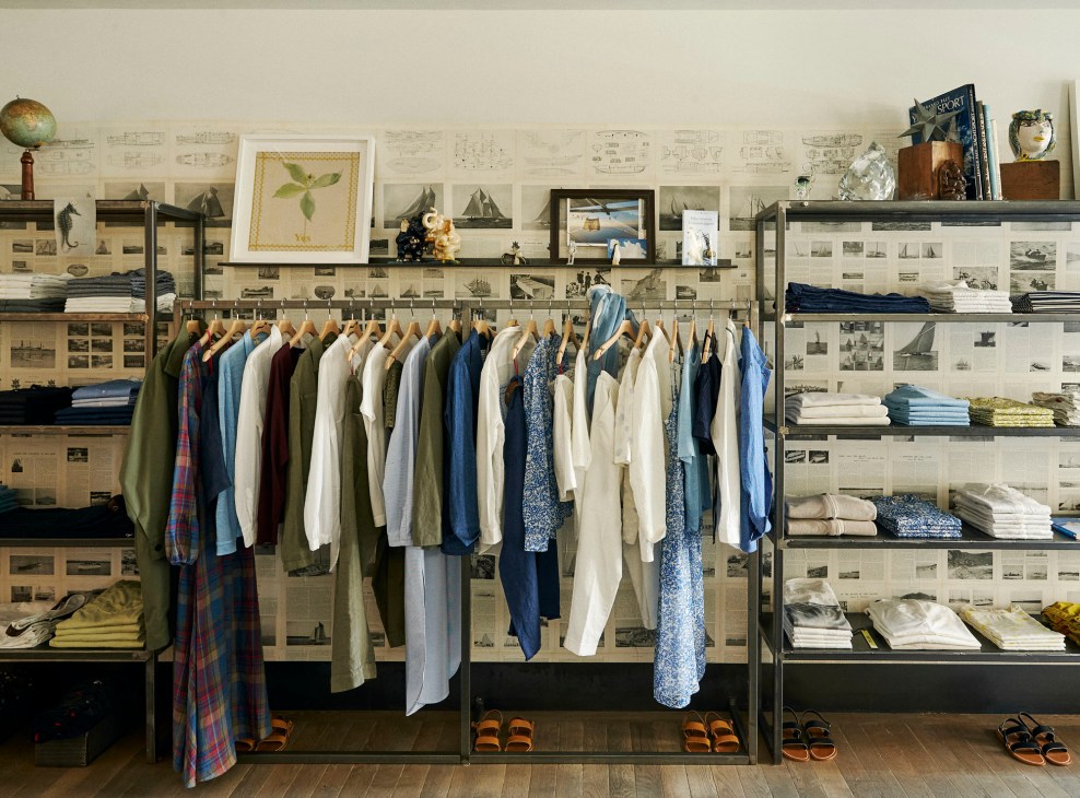 Open wardrobe system with hanging clothes and folded items on shelves against wallpapered walls