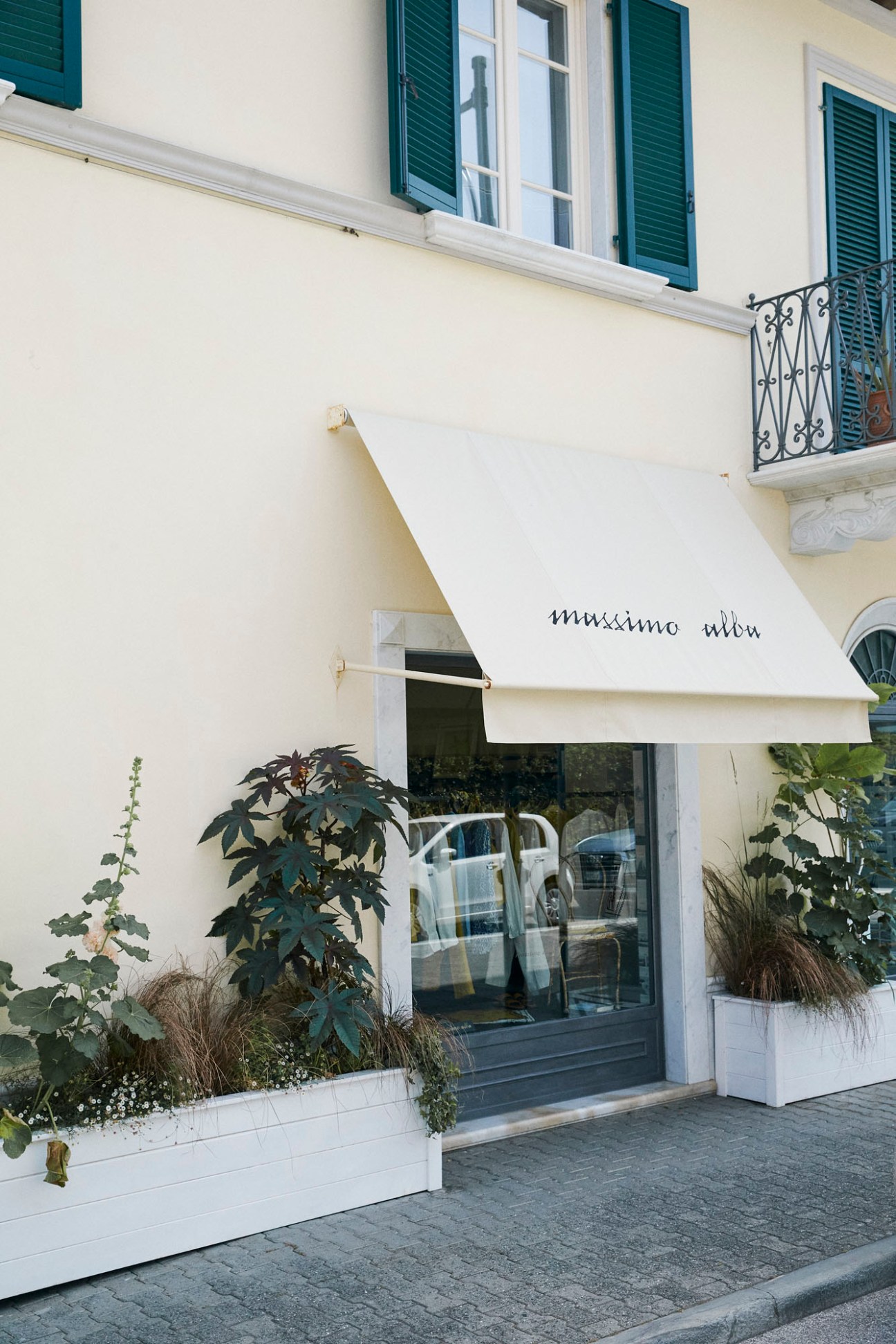 Exterior of Massimo Alba boutique in Forte dei Marmi with cream awning, green shutters and white planters