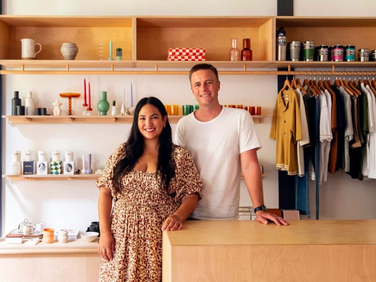 Two people standing behind counter in Kind Curations store with shelving displaying products and clothing rack