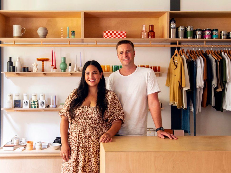 Two people standing behind counter in Kind Curations store with shelving displaying products and clothing rack