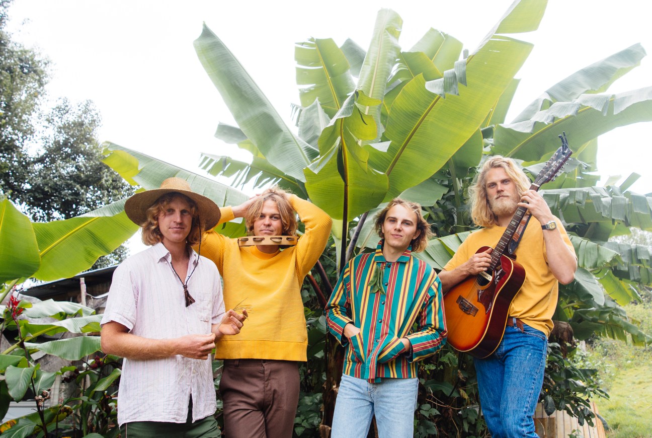 Babe Rainbow band members pose with instruments against large green banana leaves in a tropical garden setting.