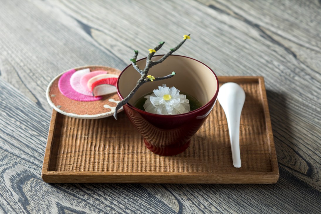 Elegant Japanese tea presentation with white flower floating in red lacquer bowl on wooden tray