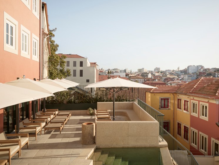 Rooftop terrace with wooden loungers, umbrellas and small pool overlooking colorful Portuguese buildings