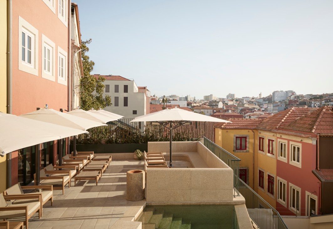 Rooftop terrace with wooden loungers, umbrellas and small pool overlooking colorful Portuguese buildings