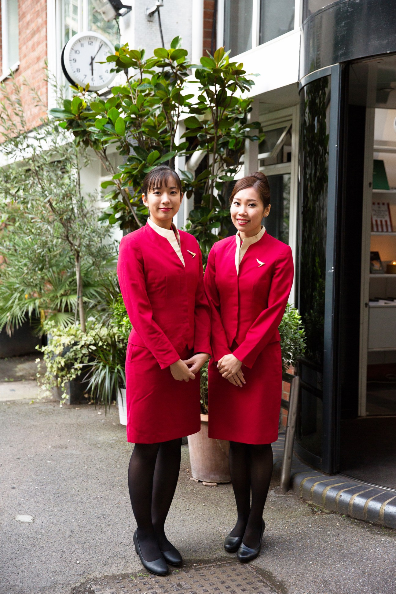 Two women in red uniforms with small airline pins standing together outdoors