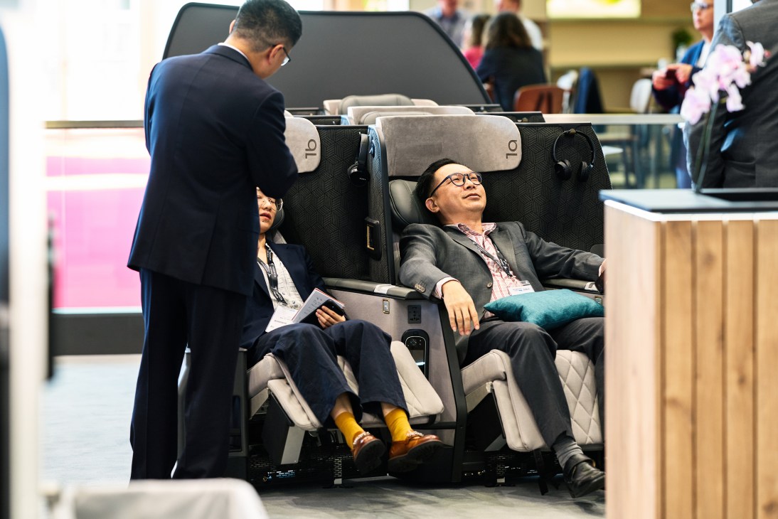 Two business professionals testing a premium airline seat with integrated in-flight entertainment display at the Aircraft Interiors Expo in Hamburg