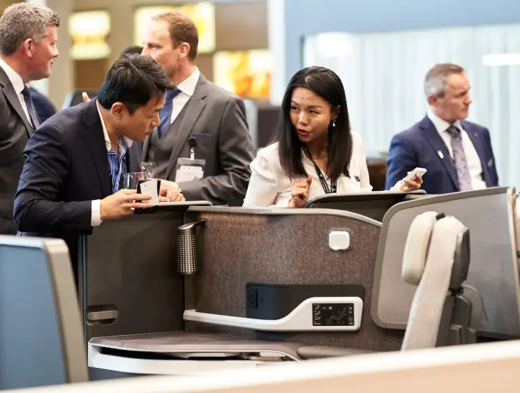 Two business professionals in suits examining airline seat displays at an aviation trade show