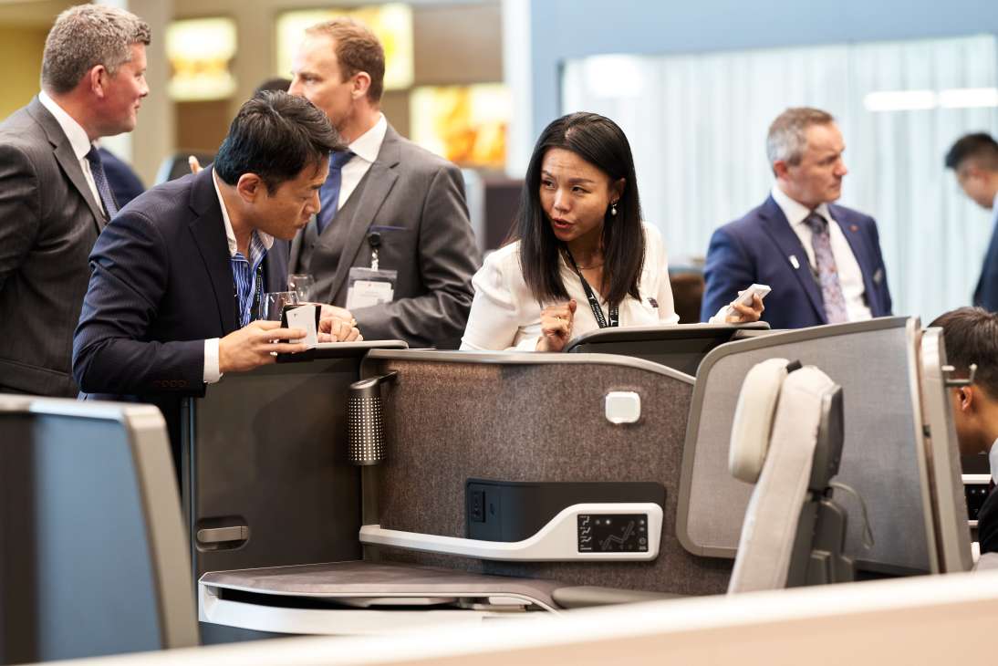 Two business professionals in suits examining airline seat displays at an aviation trade show