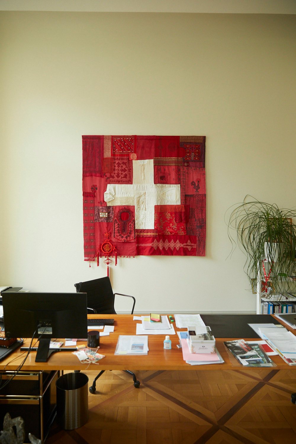 Modern office with red and white Swiss flag textile artwork on wall above wooden desk with papers