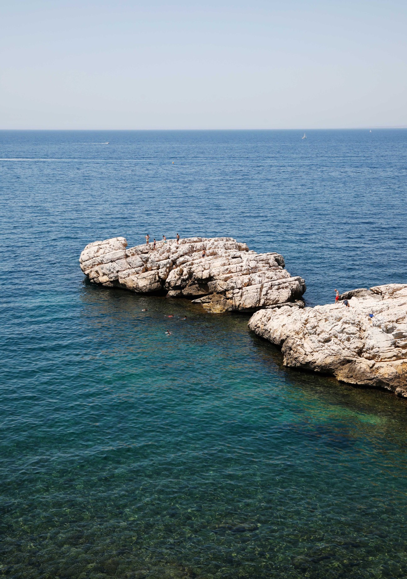 Swimmers enjoying crystal clear Mediterranean water near white limestone rocks on the coast