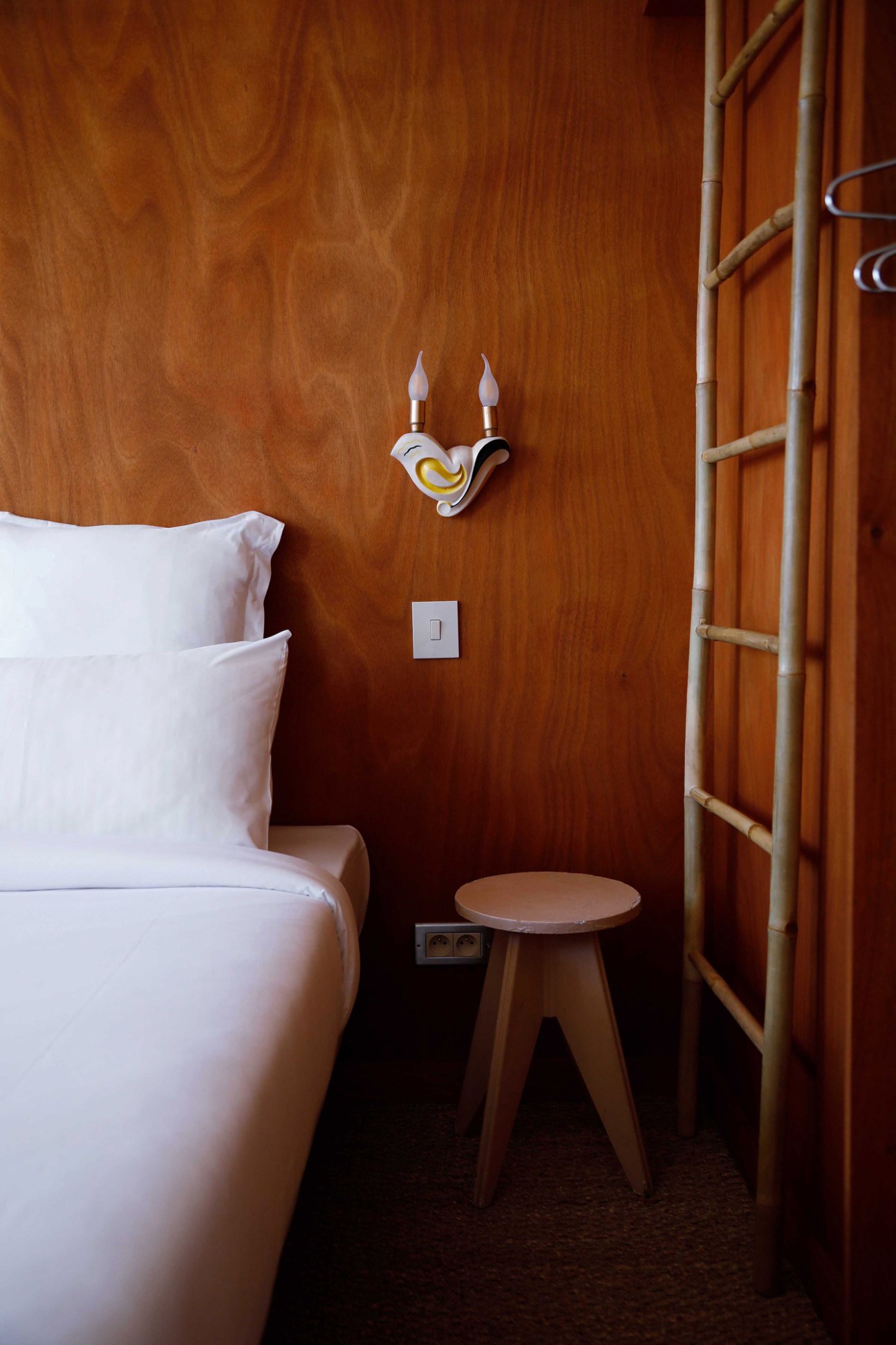 Modern hotel bedroom with wood-paneled walls, white bedding, wall sconce, and ladder
