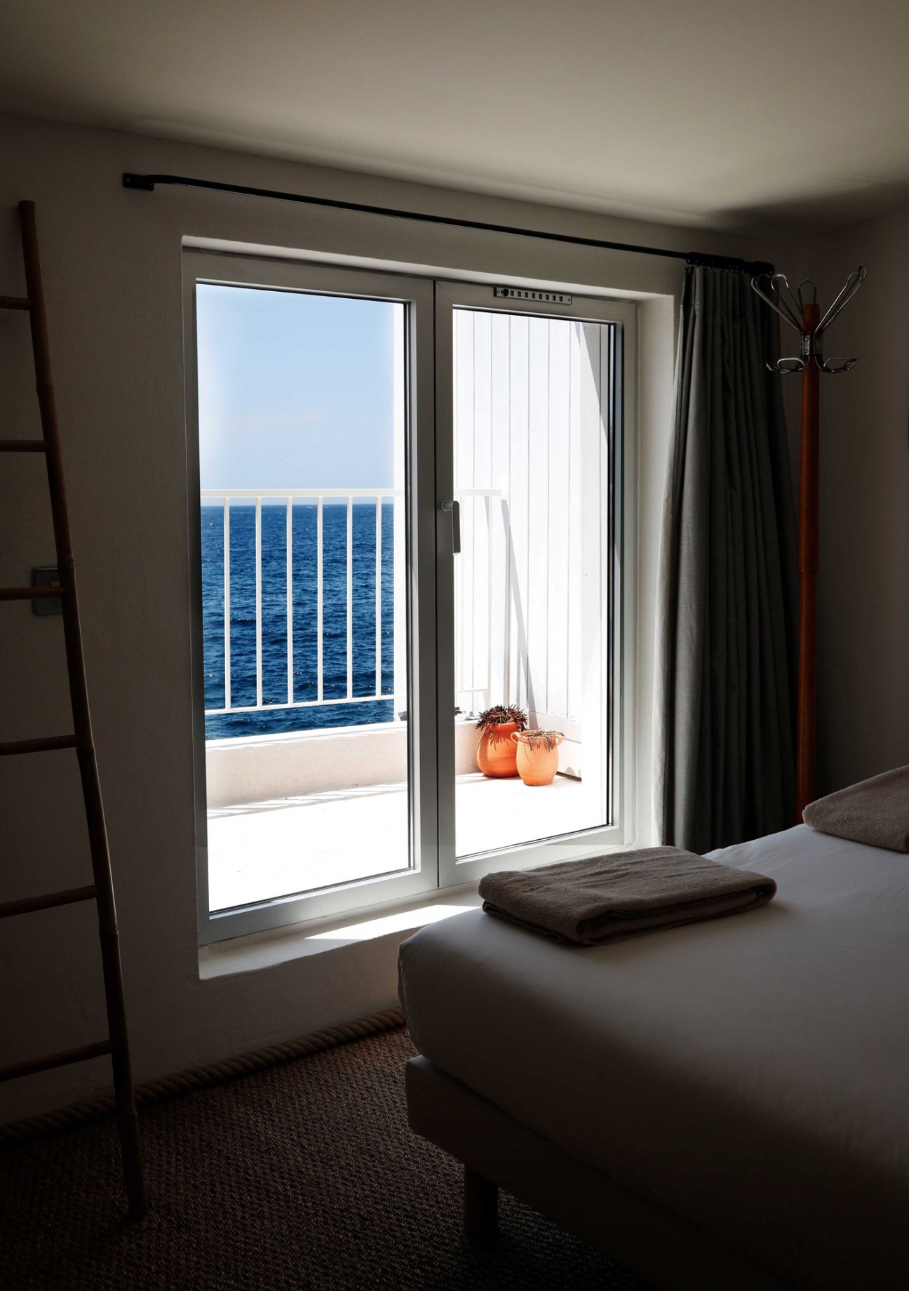 Simple hotel room interior with wooden bed and large window overlooking Mediterranean Sea