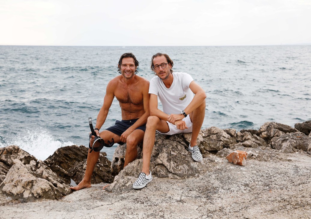 Fabrice Denizot and Greg Gassa, founders of Tuba Club, sitting on rocky Mediterranean coastline