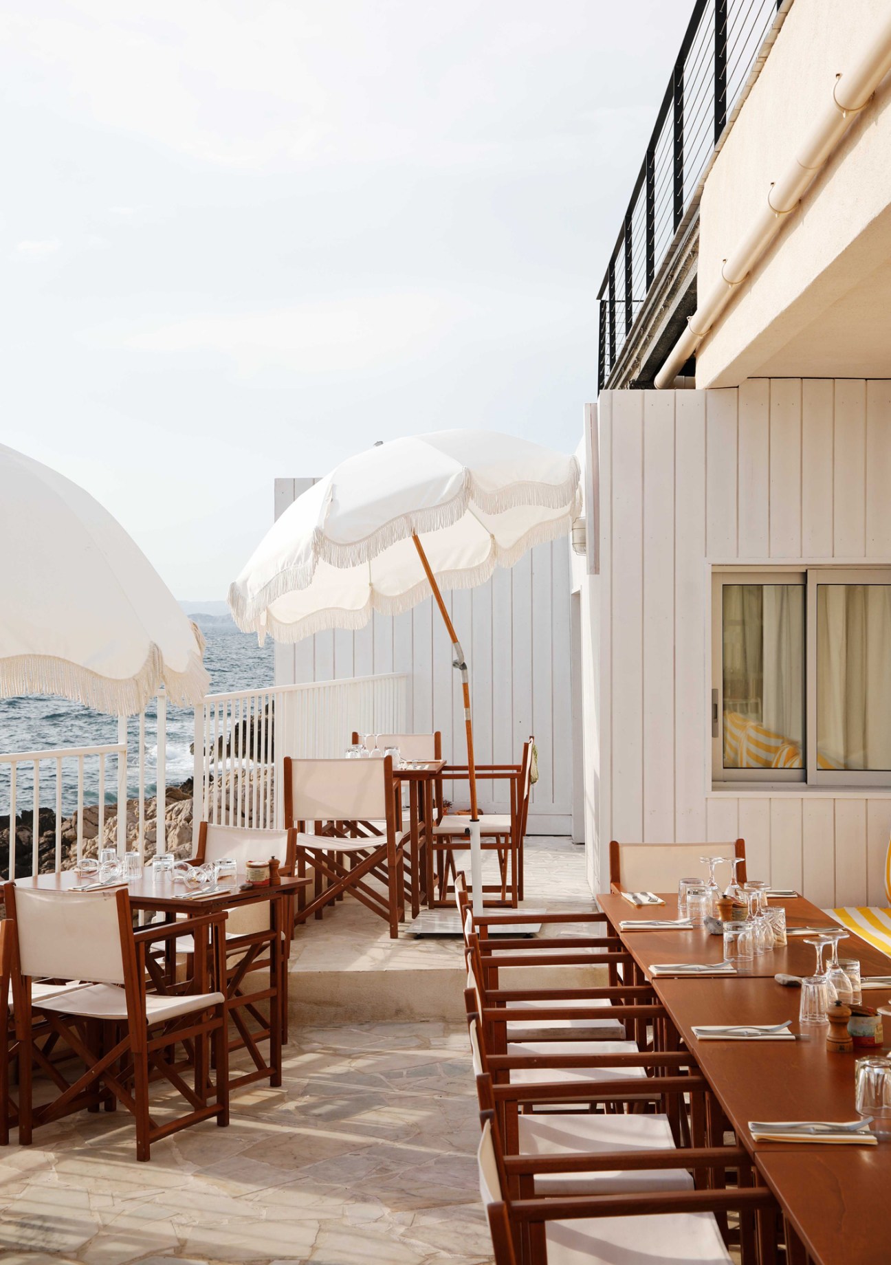 Outdoor restaurant terrace with wooden tables and chairs, white umbrellas, overlooking Mediterranean Sea at Tuba Club