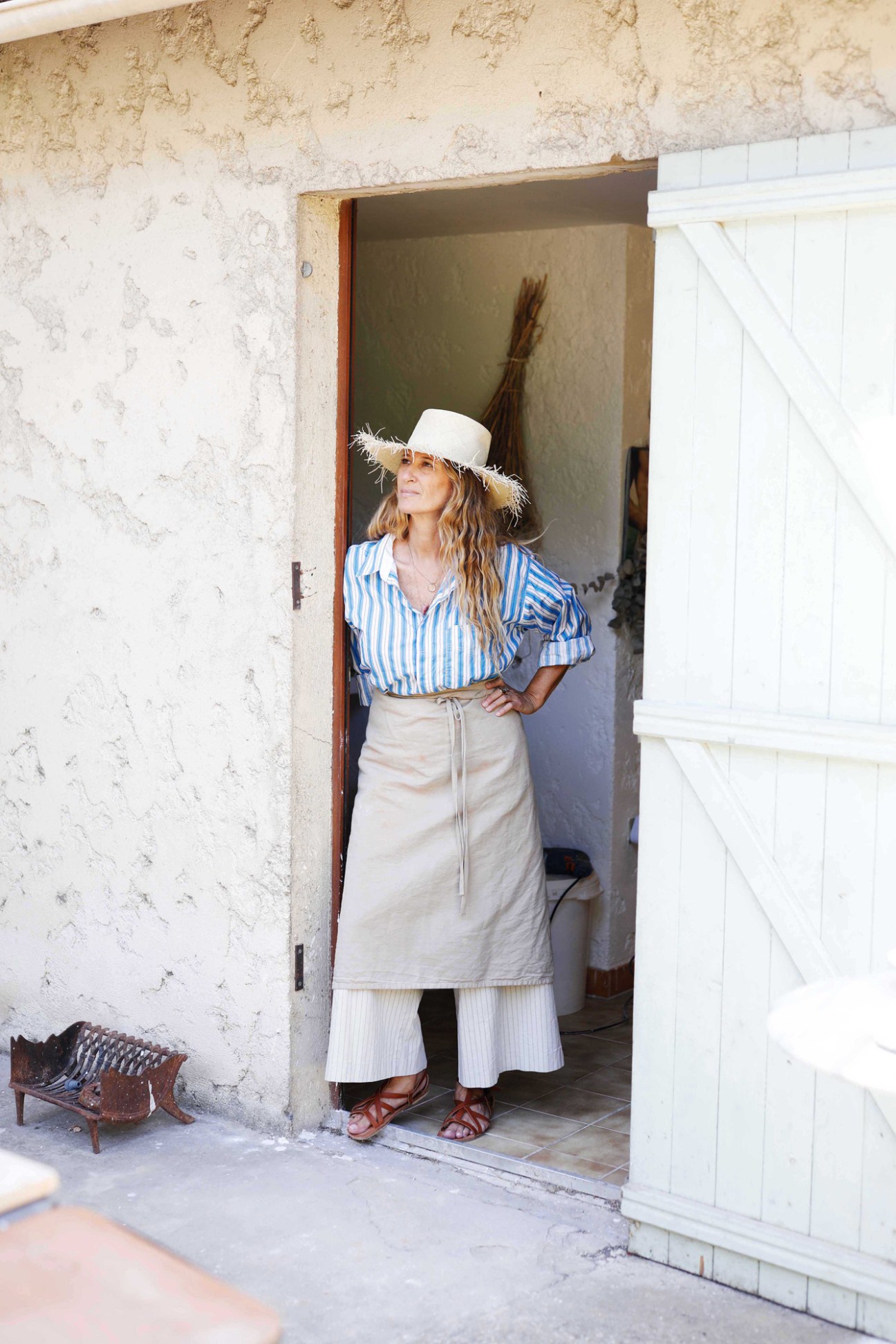 France Bocognani in striped shirt and wide-brimmed hat standing in doorway of rustic stone building