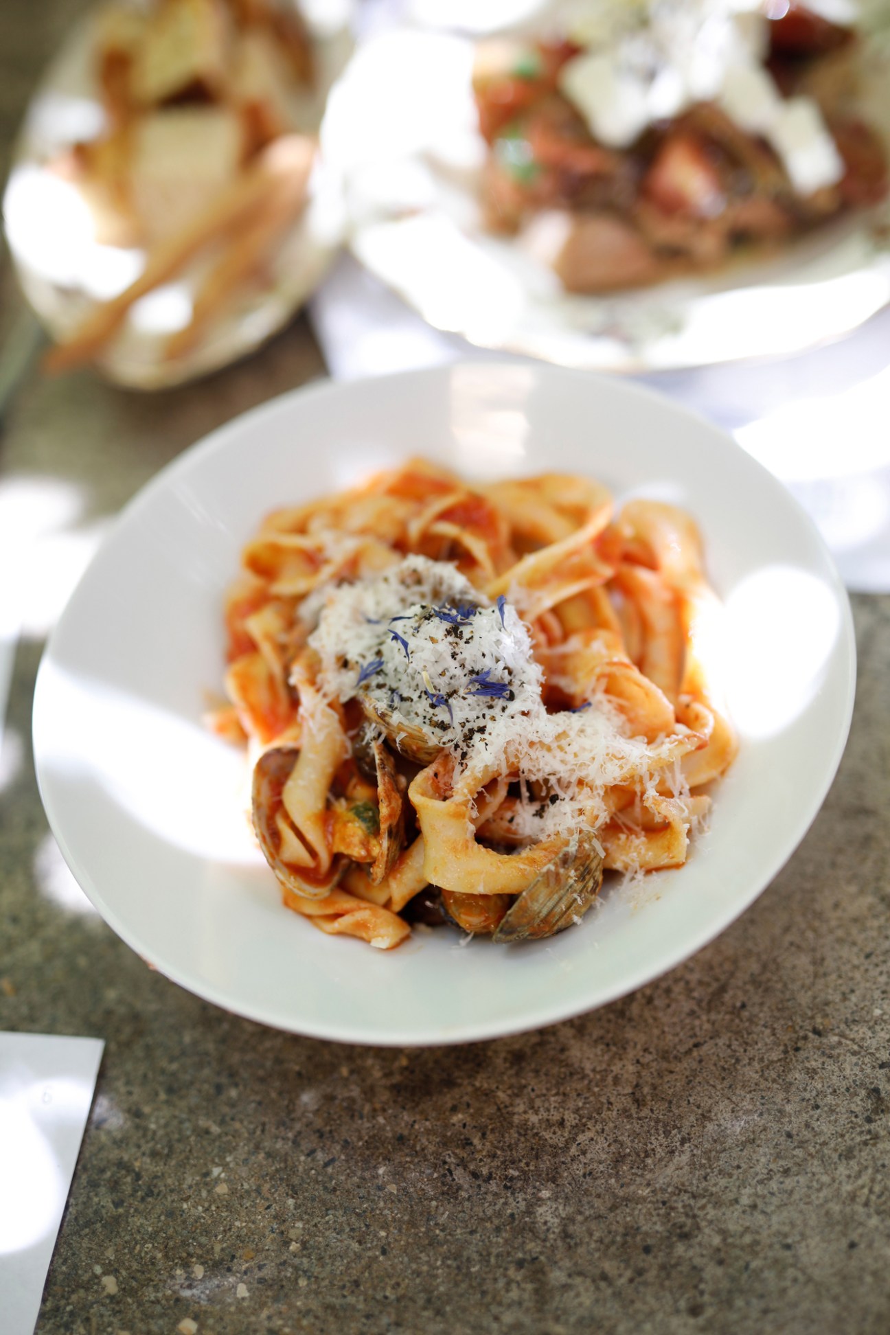 Pasta dish with fettuccine noodles, grated cheese, black pepper and purple flowers on white plate