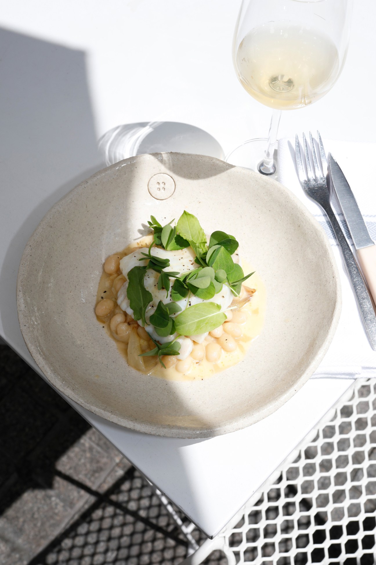 Elegant plated dish with turbot fish, white beans and microgreens on speckled ceramic plate with wine glass