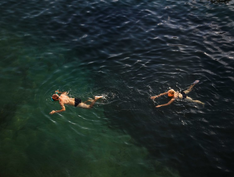 Two people swimming in dark green water viewed from above