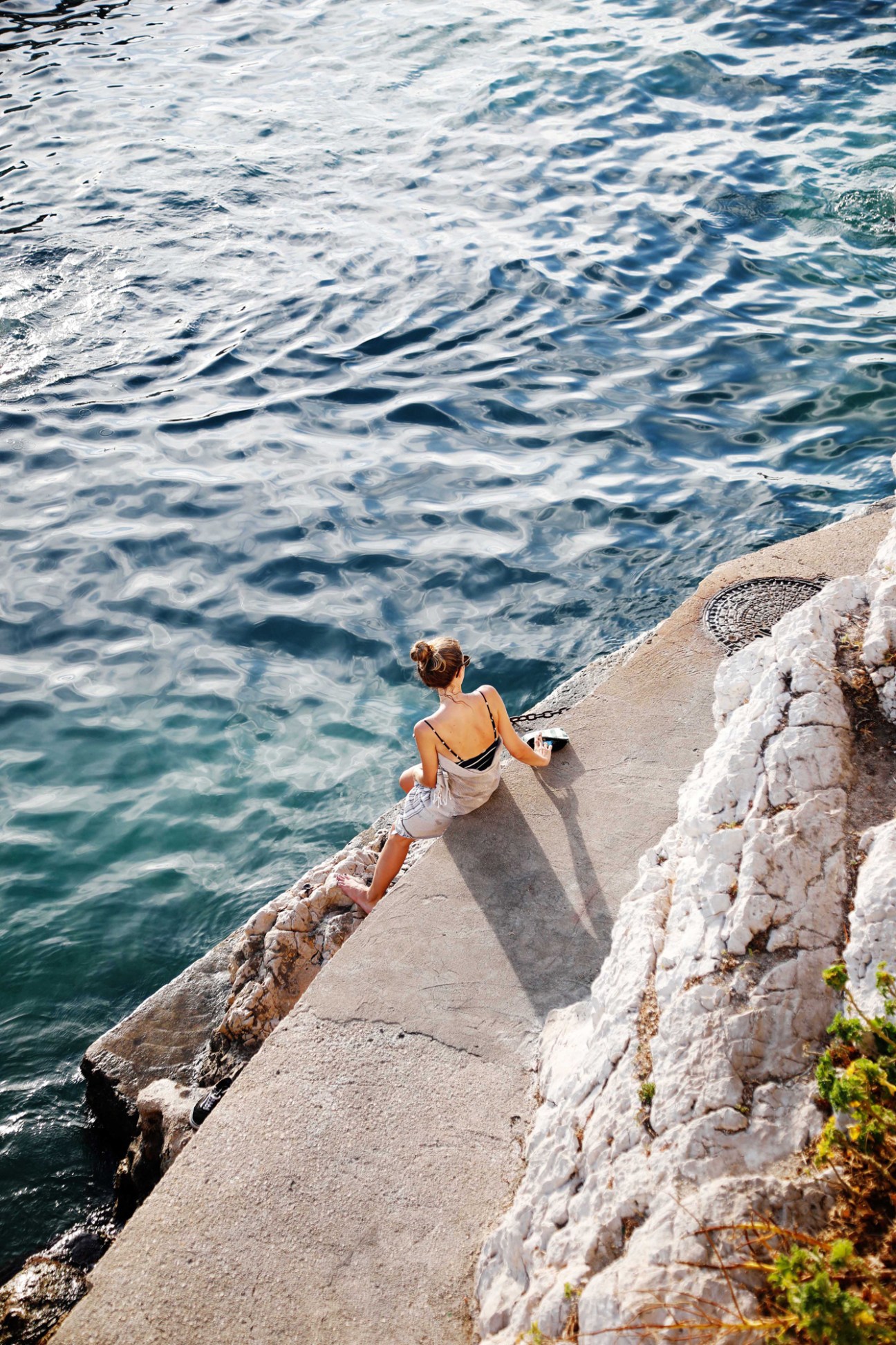 Person smoking cigarette while sitting on concrete steps overlooking Mediterranean Sea at sunset