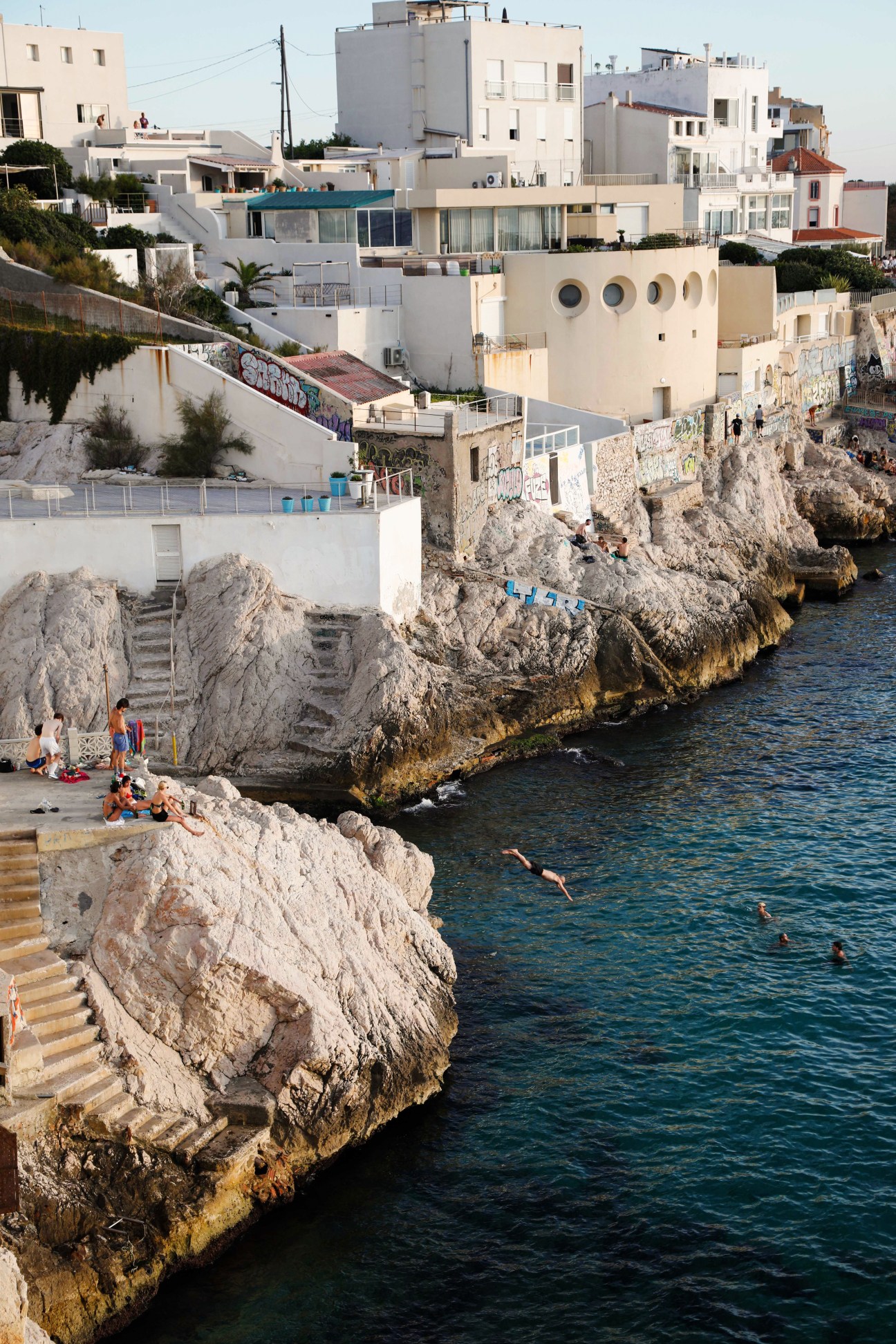 Coastal Mediterranean town with white buildings on rocky cliffs overlooking blue water where people swim